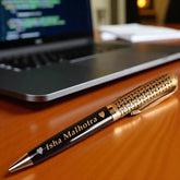 Gold and Black Name Pen - Personalized Gift | Custom Ball Pen with engraved name 'Isha Malhotra' placed on a wooden desk near a laptop.